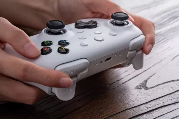 Person holding the white 8BitDo Ultimate 2 Wireless Controller on a wooden surface